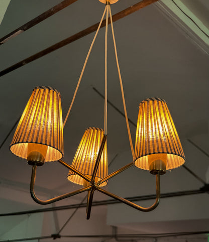 Chandelier with three illuminated lampshades hanging from a ceiling.