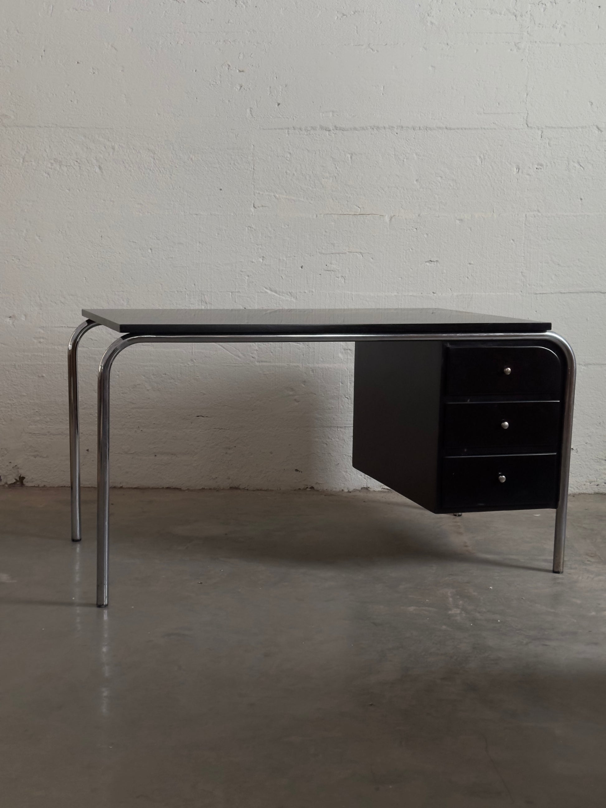 Modern black desk with metal legs against a white brick wall.