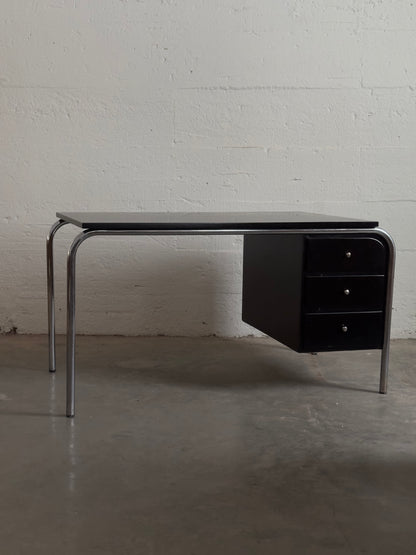 Modern black desk with metal legs against a white brick wall.