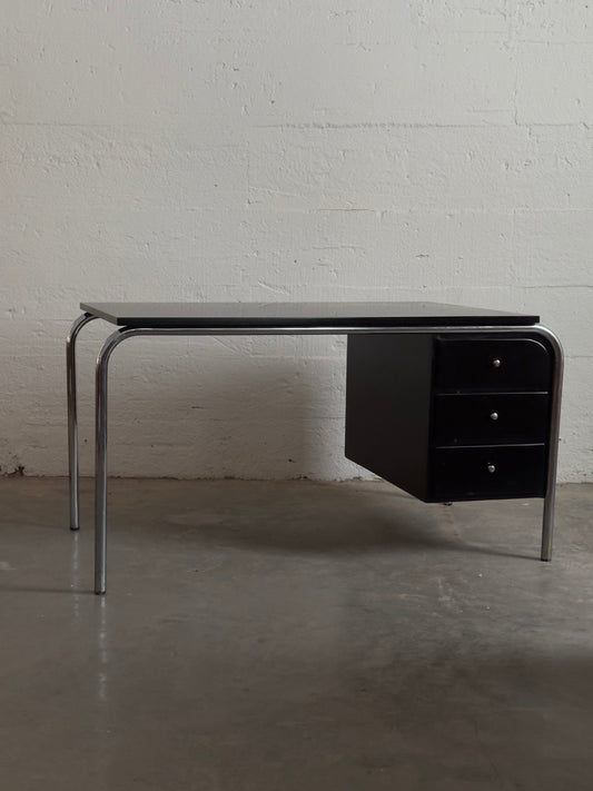 Modern black desk with metal legs against a white brick wall.