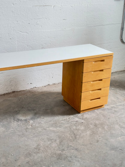 Aalto wooden desk with white top against a gray wall.