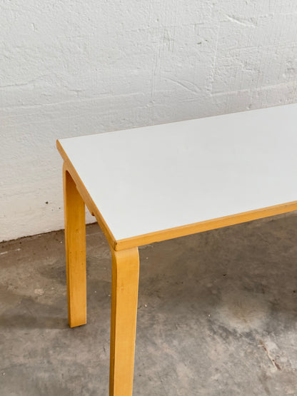 Aalto desk with a white lino top and wooden legs against a plain wall.