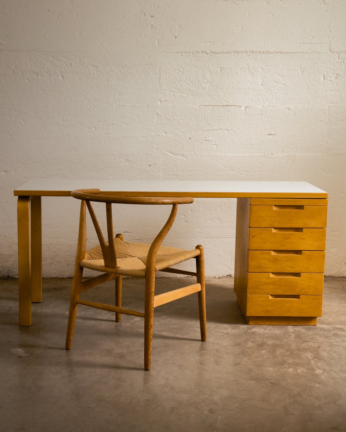 Aalto Wooden desk with drawers and chair against a white brick wall.