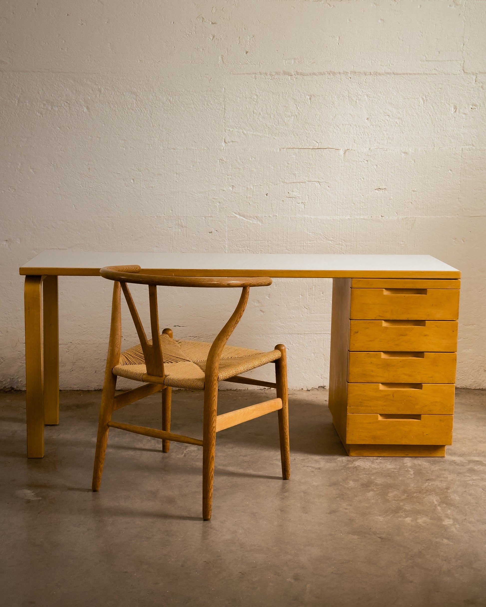 Aalto Wooden desk with drawers and chair against a white brick wall.