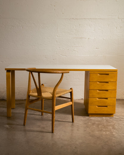 Aalto Wooden desk with drawers and chair against a white brick wall.